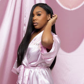 Woman in a pink satin robe against a pink curtain background wearing silky straight hair from the silk press collection at House of SIlk Hair